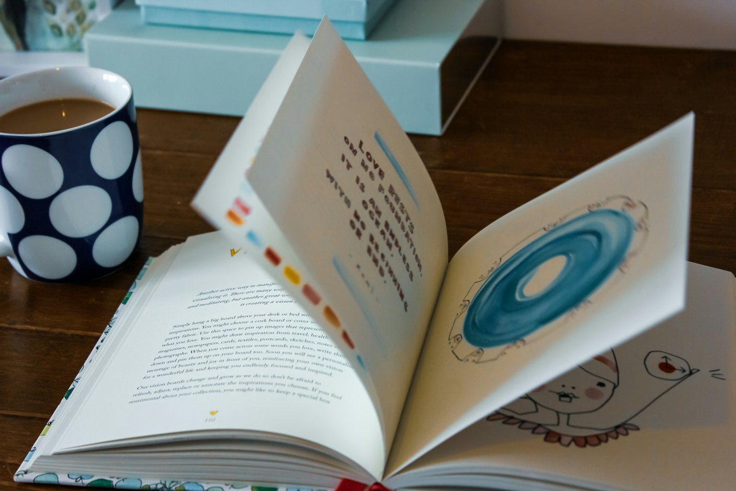 Offenes illustriertes Buch und eine gepunktete Tasse auf einem Tisch.